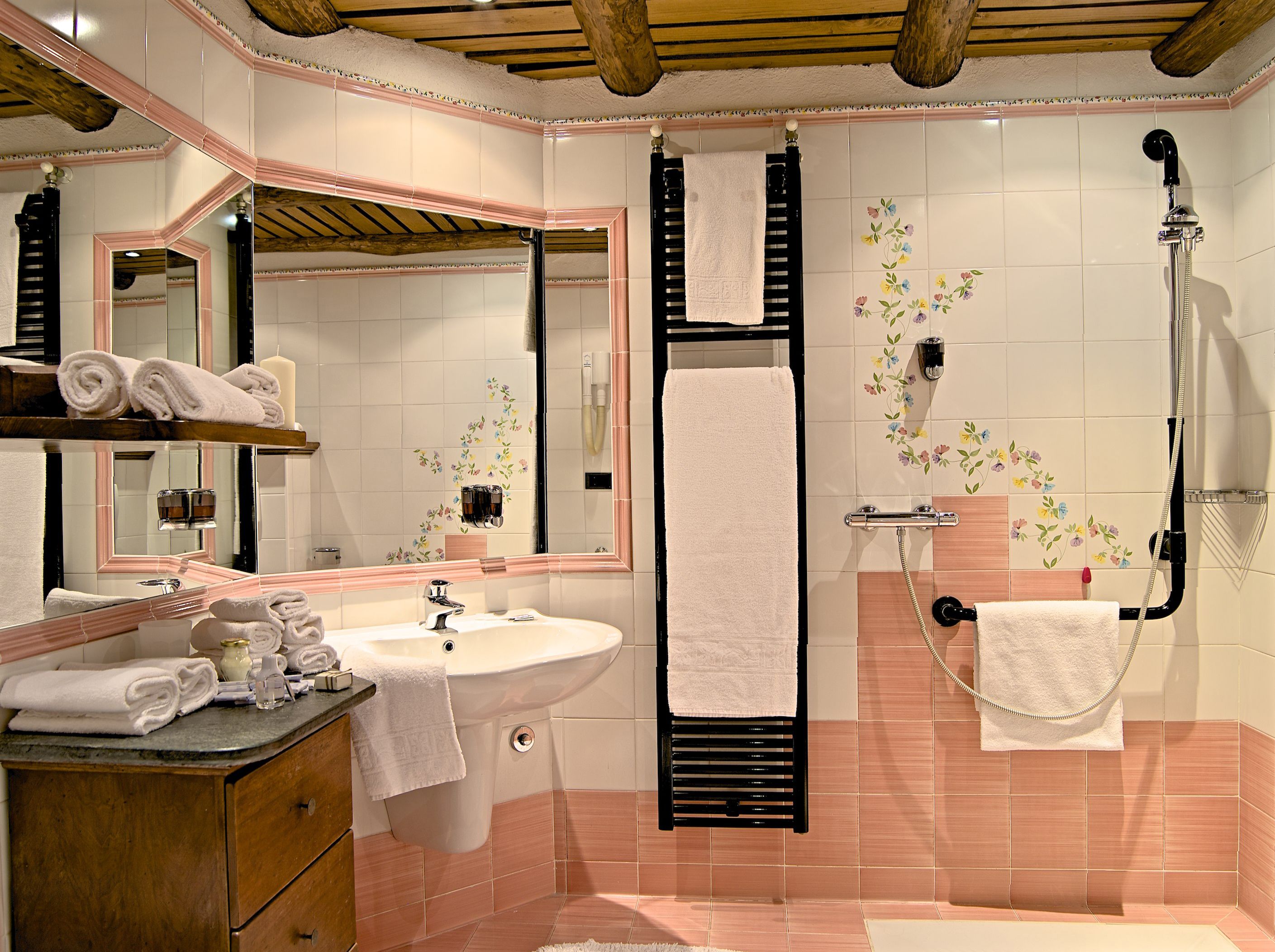A bathroom with a sink, mirror, towel rack, shower, and wooden ceiling beams.