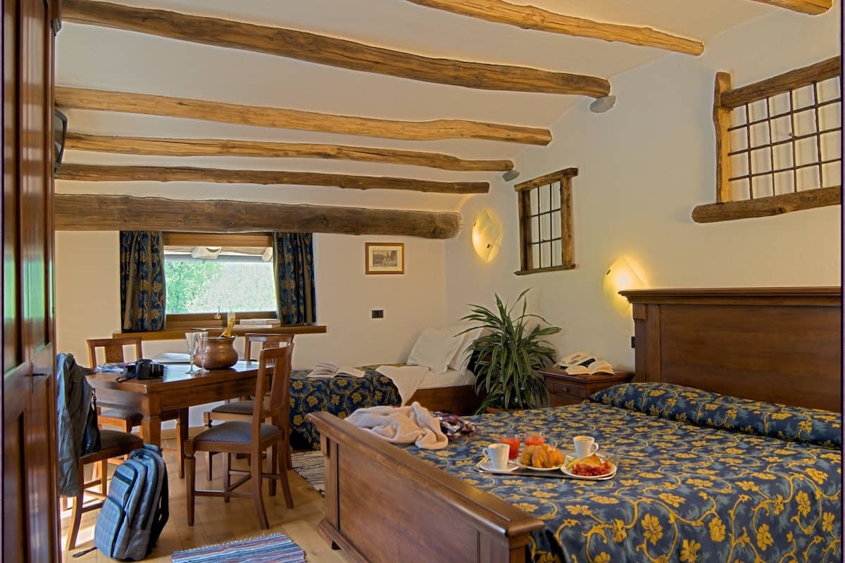 Une pièce chaleureuse avec un plafond en bois, un lit recouvert d’une literie à motifs floraux, une table à manger avec des chaises et une fenêtre avec des rideaux.