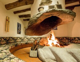 Una chimenea de piedra con fuego encendido, un banco de madera y un sofá estampado con motivos florales.
