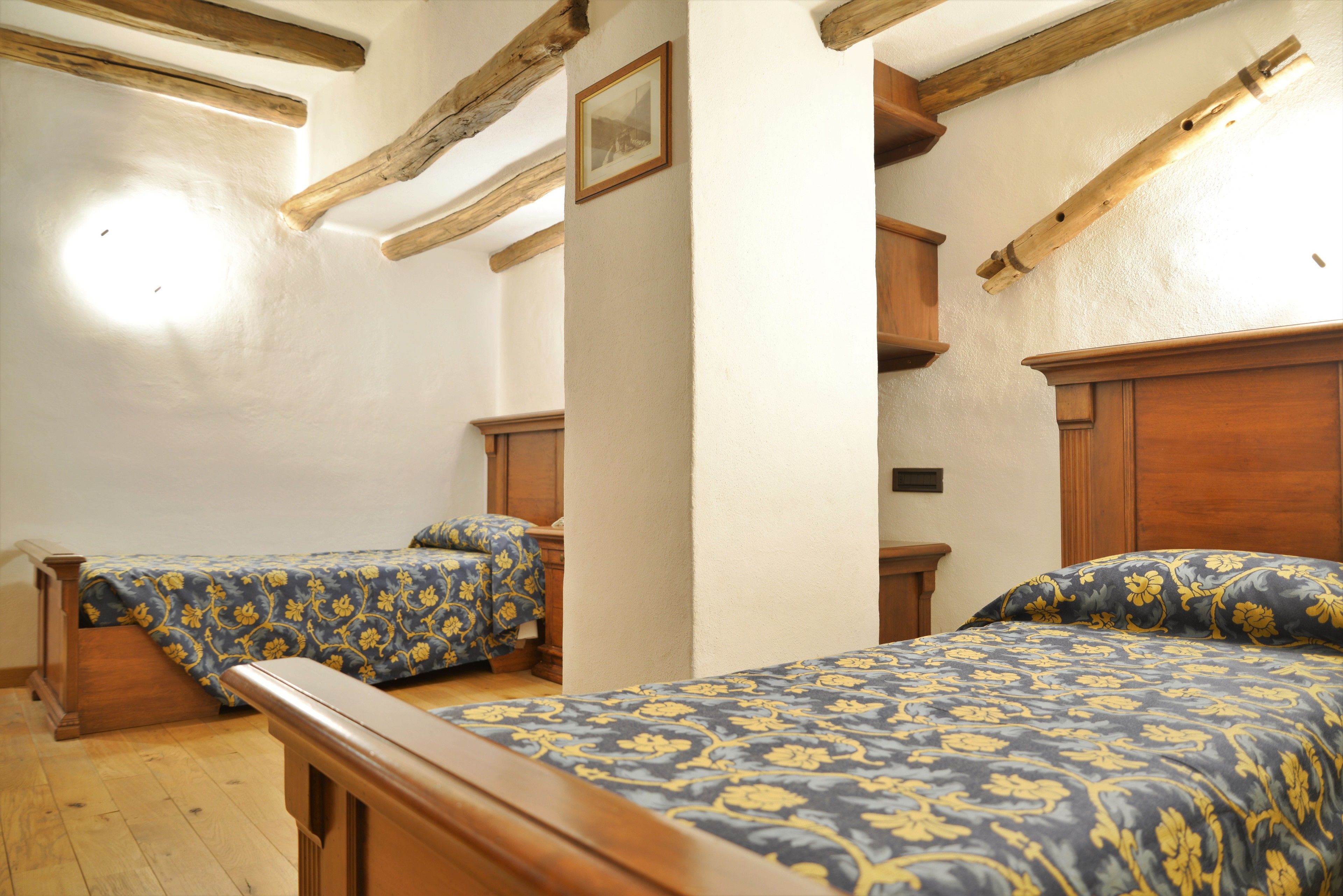 A room with two wooden beds, a wooden bench, and a white wall with a framed picture.