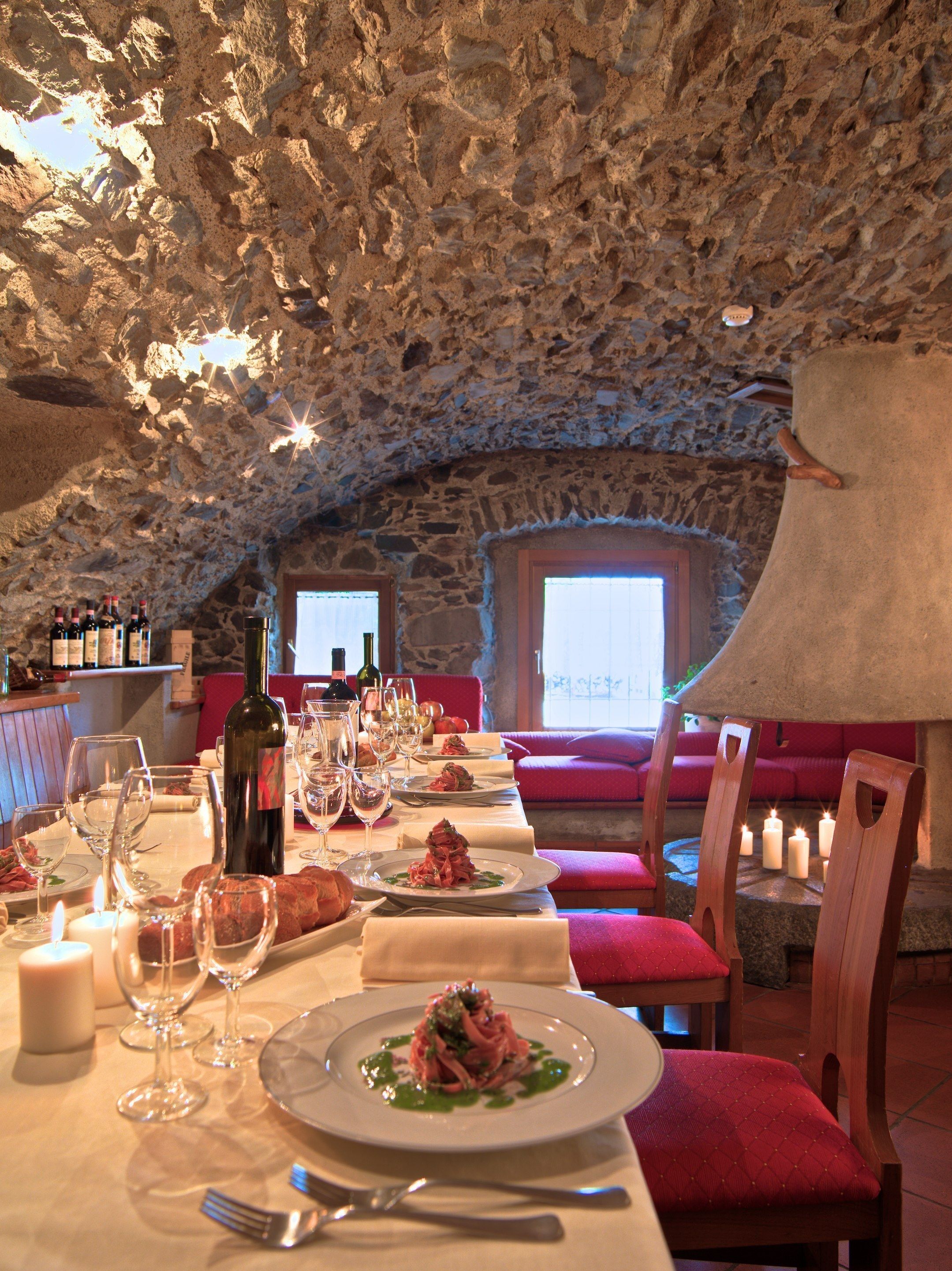 A restaurant with a stone ceiling, red upholstered seating, and a long table set for dining.