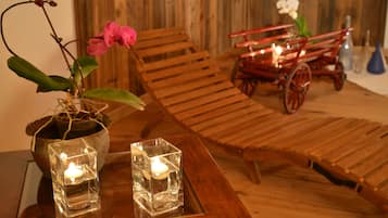 A wooden table with two glass candle holders, a potted orchid, and a vintage red carriage with lights.
