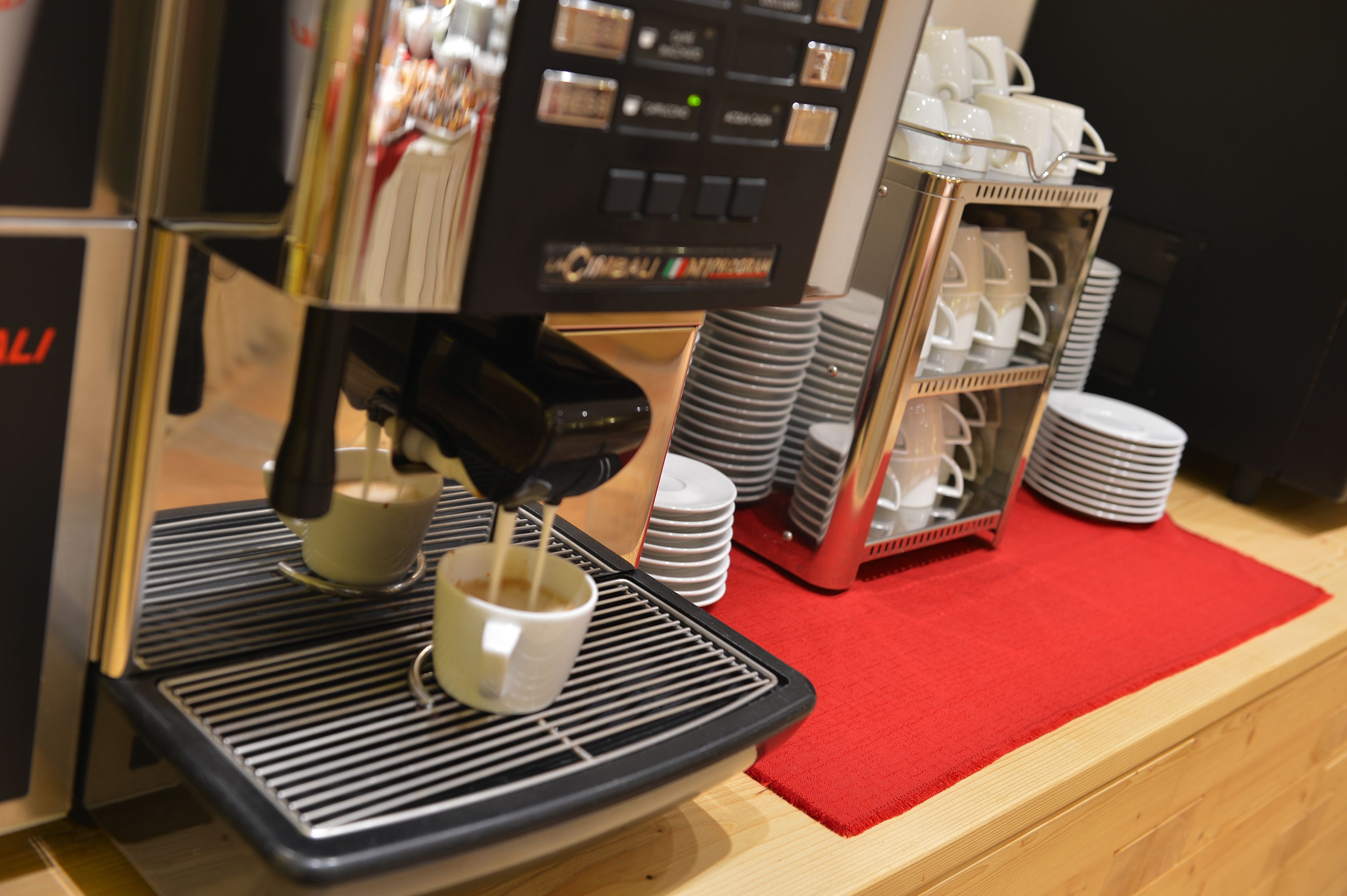 A coffee machine dispensing coffee into a cup, a stack of plates, and a tray with a red mat.