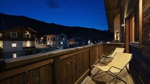 A wooden balcony with two lounge chairs, overlooking a street with buildings and a mountain in the background. - Hotel Meeting (Livigno)