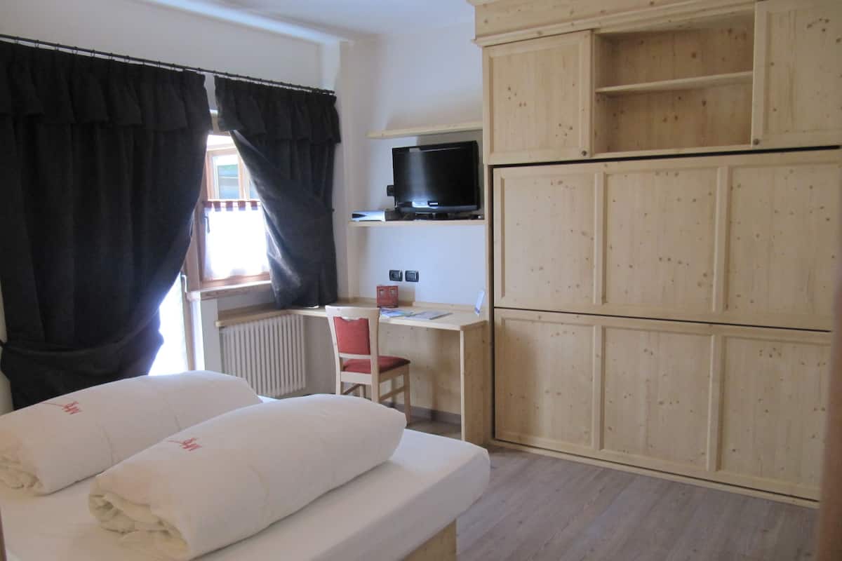 A bedroom with a bed, a desk, and a television.