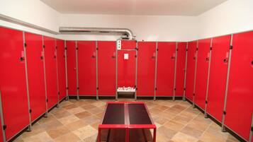 Una hilera de taquillas rojas con un conducto de ventilación central, una mesa roja en el centro y un piso de baldosas.