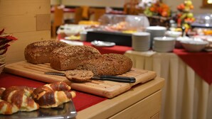A buffet table with various breads and pastries, a cutting board, and a knife. - Hotel Meeting (Livigno)
