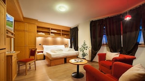 A cozy room with a bed, a red sofa, a small table, and wooden cabinets. - Hotel Meeting (Livigno)