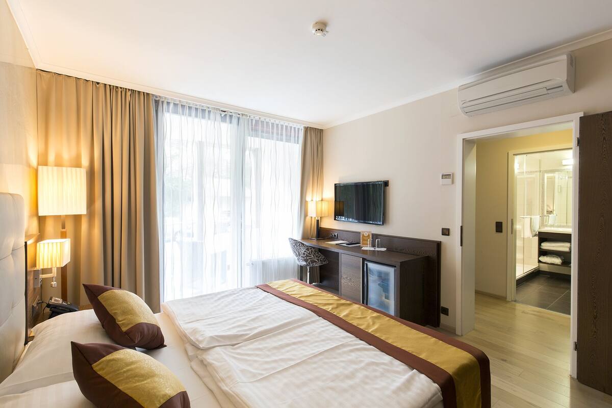 Ein Hotelzimmer mit einem großen Bett, einem Schreibtisch mit Stuhl, einem Fernseher und einem durchgegangene Tür sichtbaren Badezimmer.