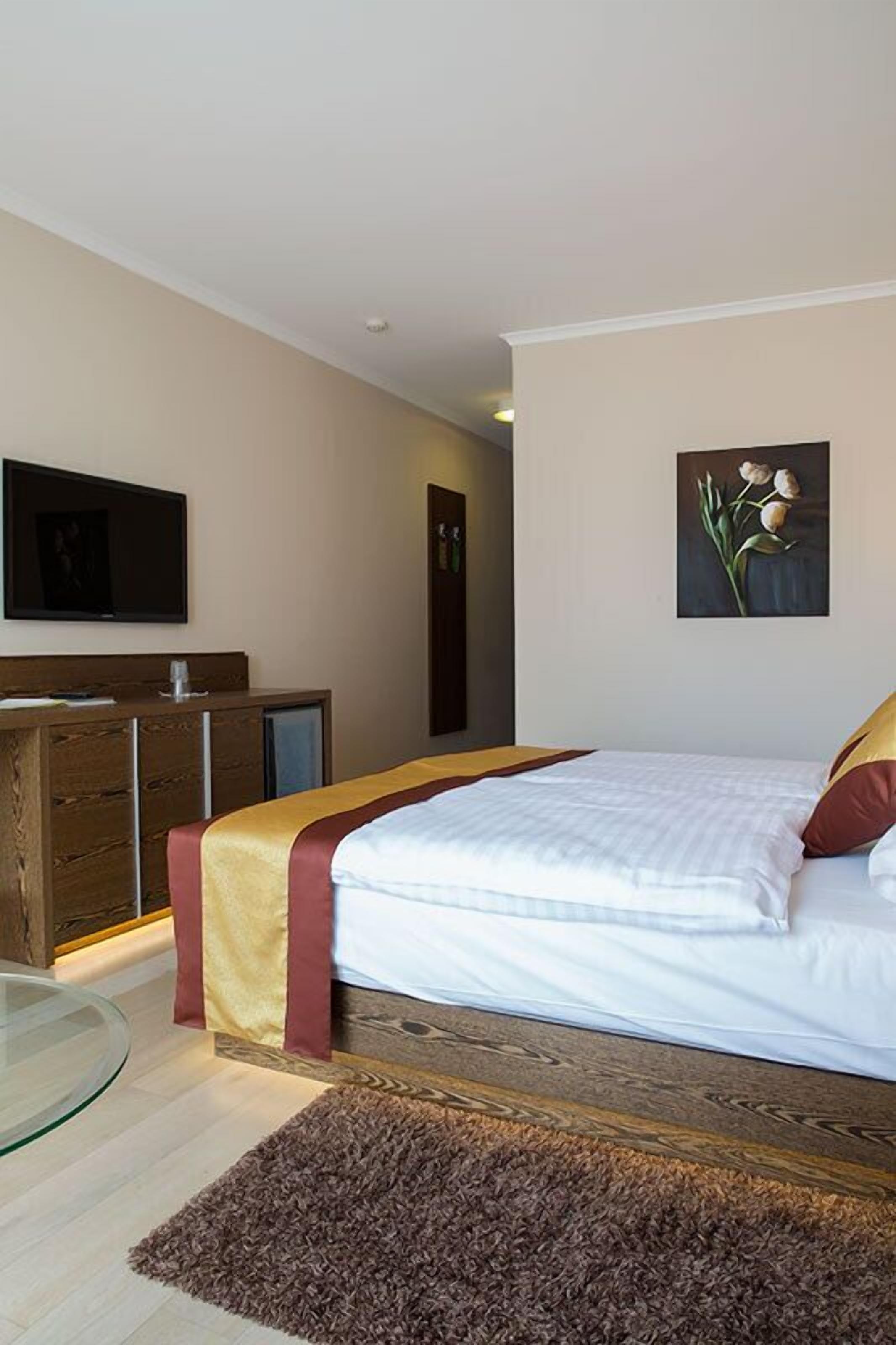 Ein Schlafzimmer mit einem Bett, einer Holzkommode, einem Glastisch und einem Bild an der Wand.