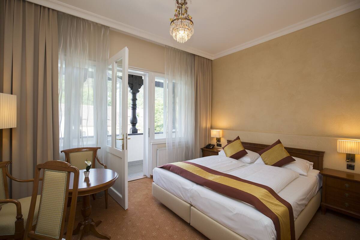 Ein Hotelzimmer mit Bett, Nachttischen, einem Schreibtisch mit Stühlen und einer Chandelier.
