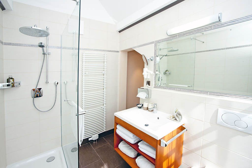 A modern bathroom with a glass shower enclosure, a white sink with a wooden vanity, and a large mirror.