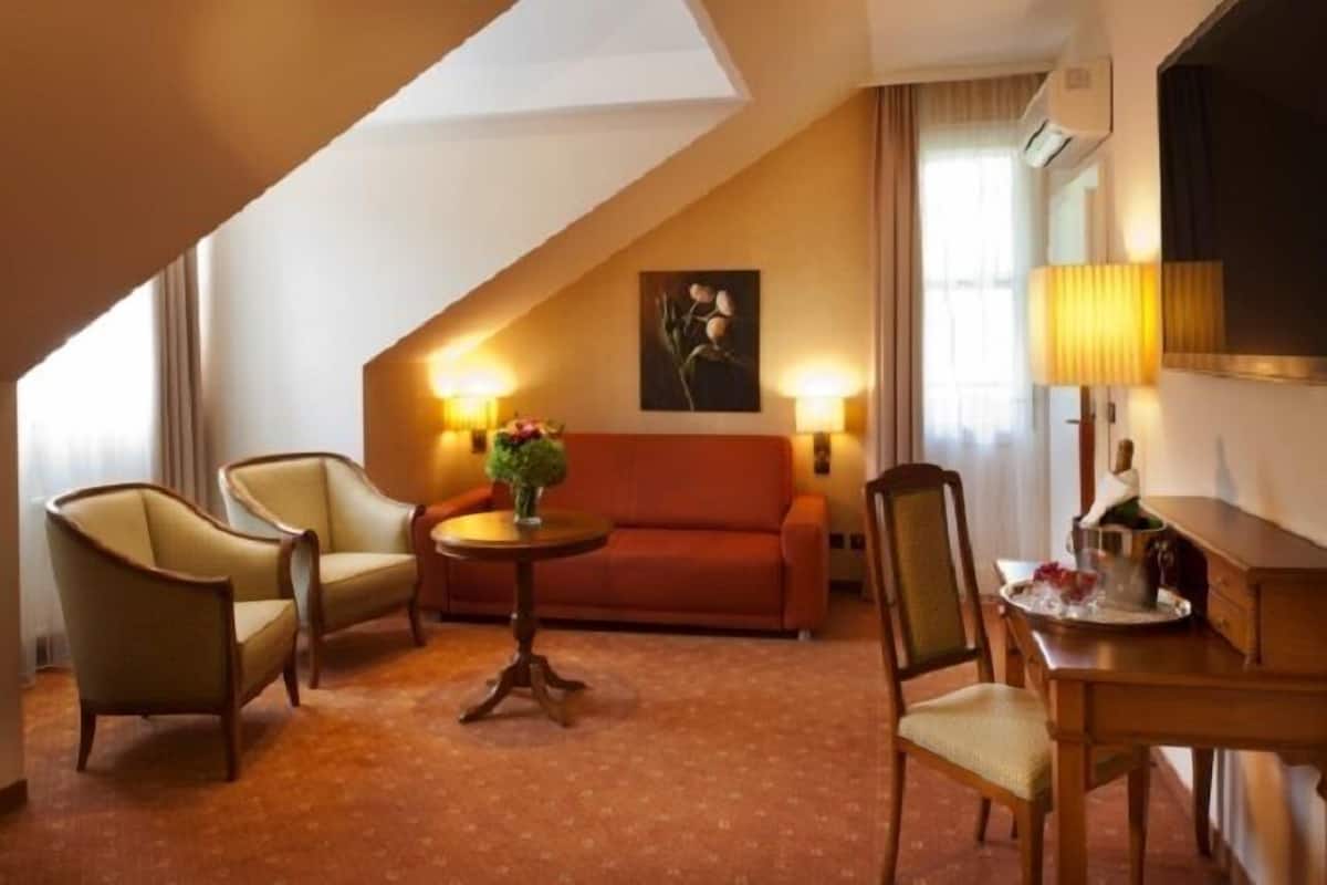 Ein Hotelzimmer mit einer Couch, zwei Sesseln, einem kleinen Tisch mit einer Vase, einer Lampe und einem Fernseher.