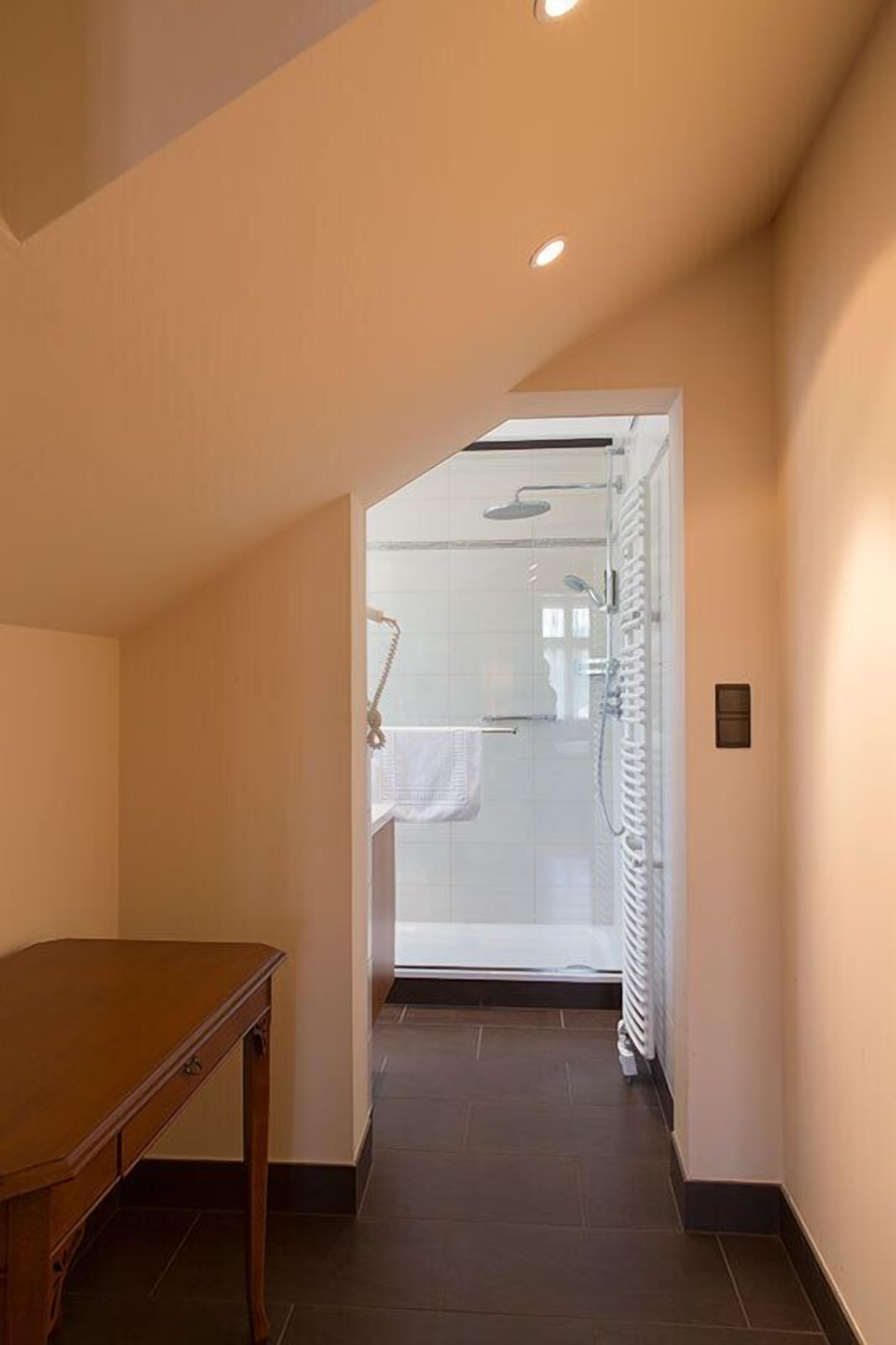 Un pasillo con una mesa de madera, una cabina de ducha de vidrio y un radiador blanco.