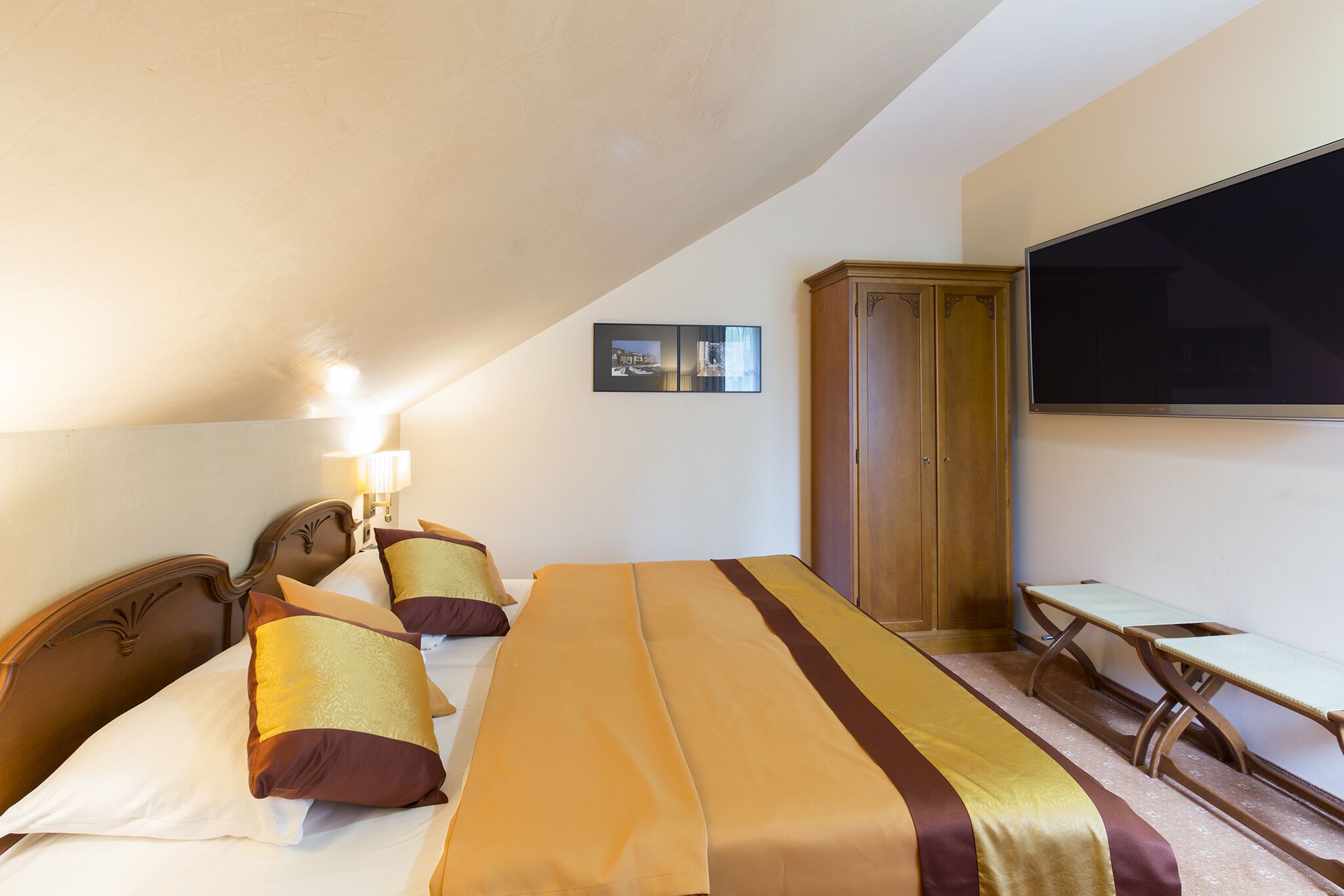 A hotel room with a large bed, two bedside tables, a wooden wardrobe, a flat-screen TV, and a framed picture on the wall.