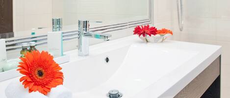 A modern bathroom with a large mirror, two sinks, a shower, and a wooden vanity.