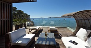 A deck with white cushioned seating, a glass-top table, and a bottle of wine. - Hostellerie La Farandole (Sanary-sur-Mer)