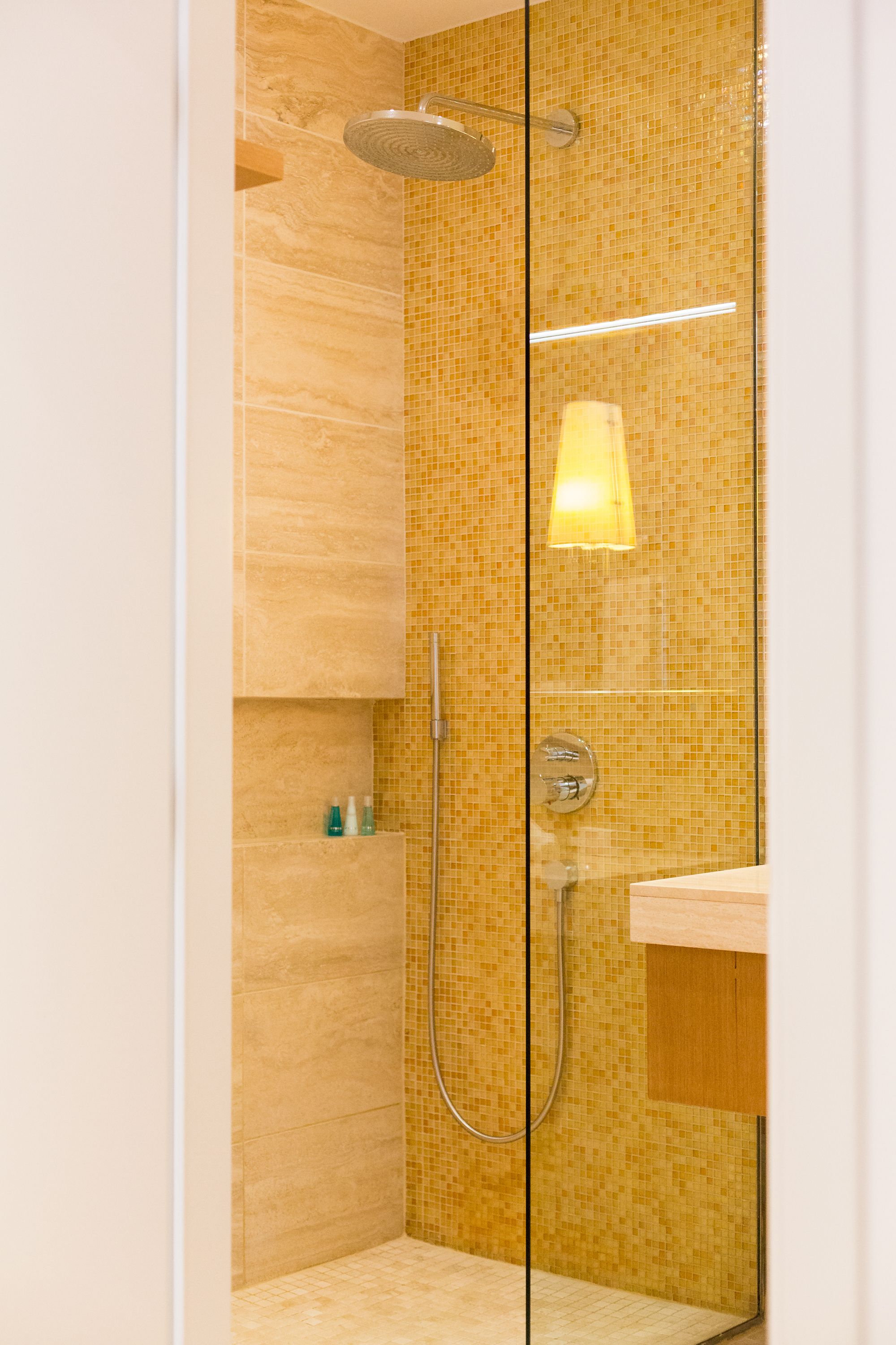 A modern shower with a glass door, a handheld showerhead, and a wall-mounted faucet.