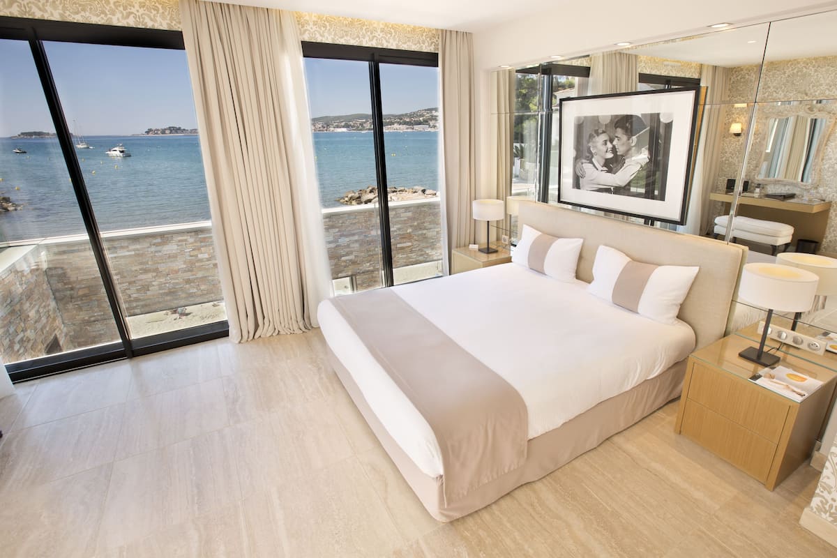 Habitación de hotel con una cama grande, una mesita de noche, un espejo y vista al mar.