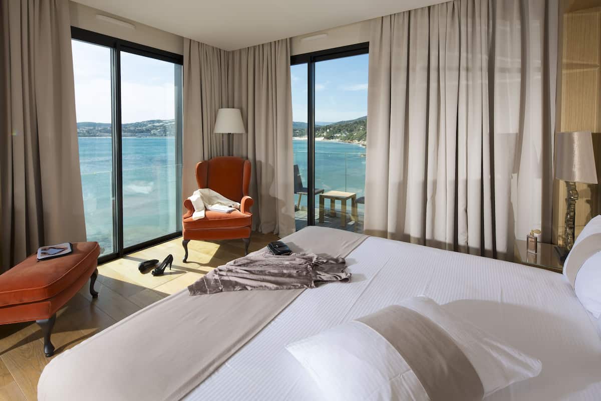 Habitación de hotel con una cama grande, una silla, una mesita y vista al mar.