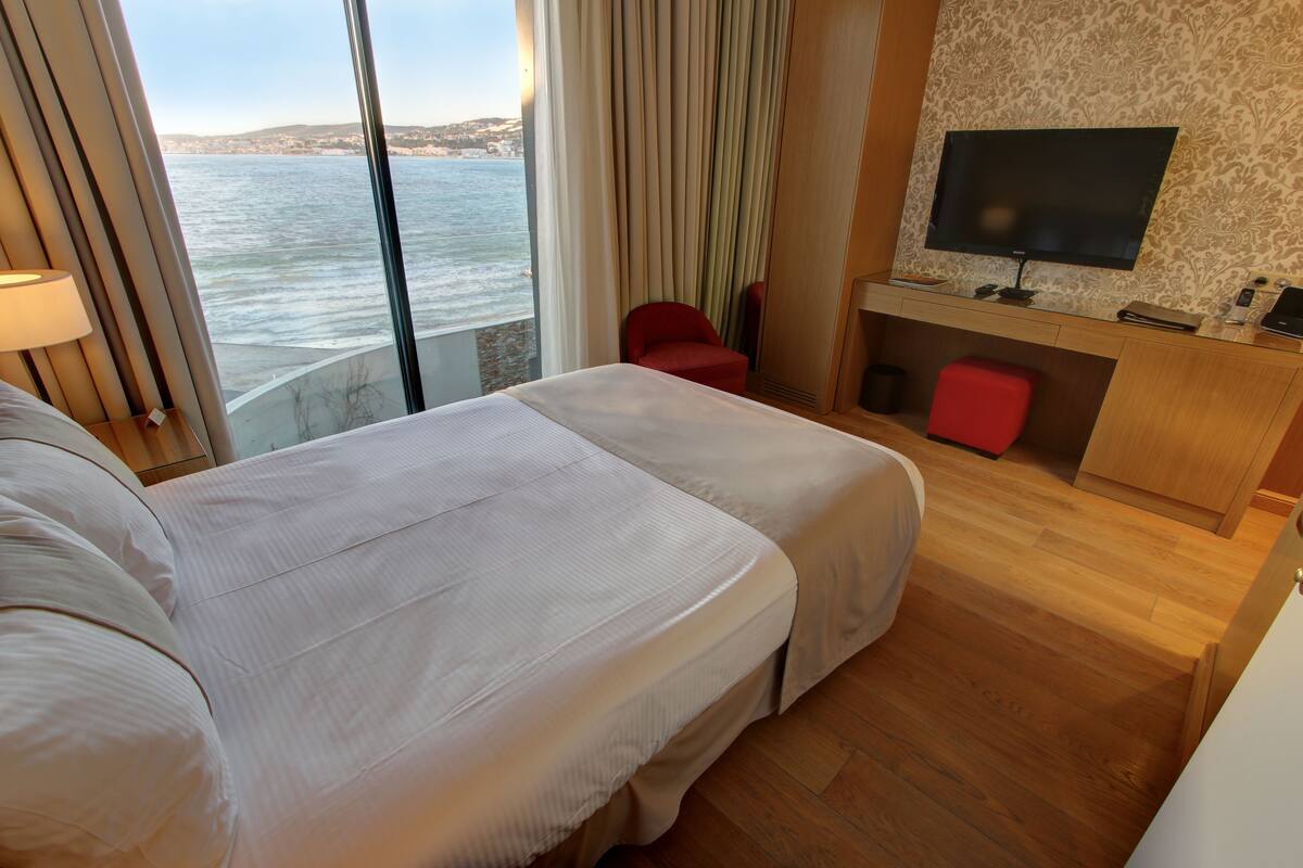 Una habitación de hotel con dos camas, televisión, escritorio y vista al mar.