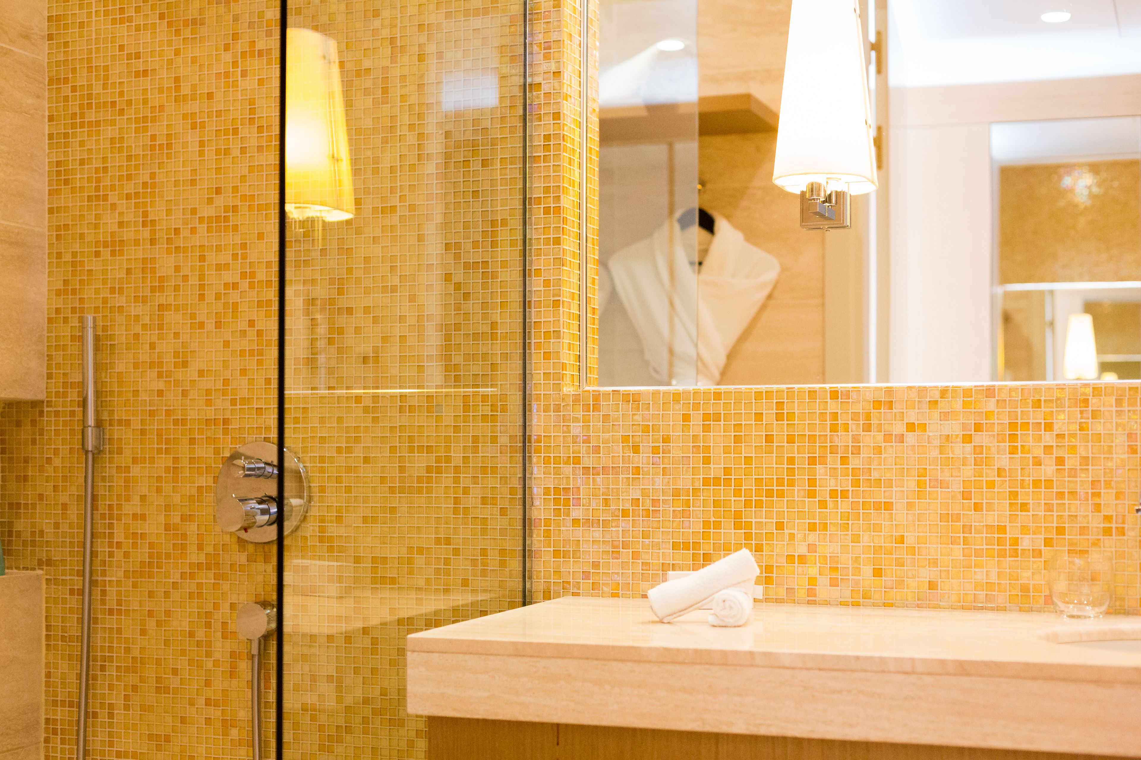 Une salle de bain avec des murs recouverts de mosaïques, une douche en verre et un meuble-lavabo en bois sur lequel est posée une serviette.