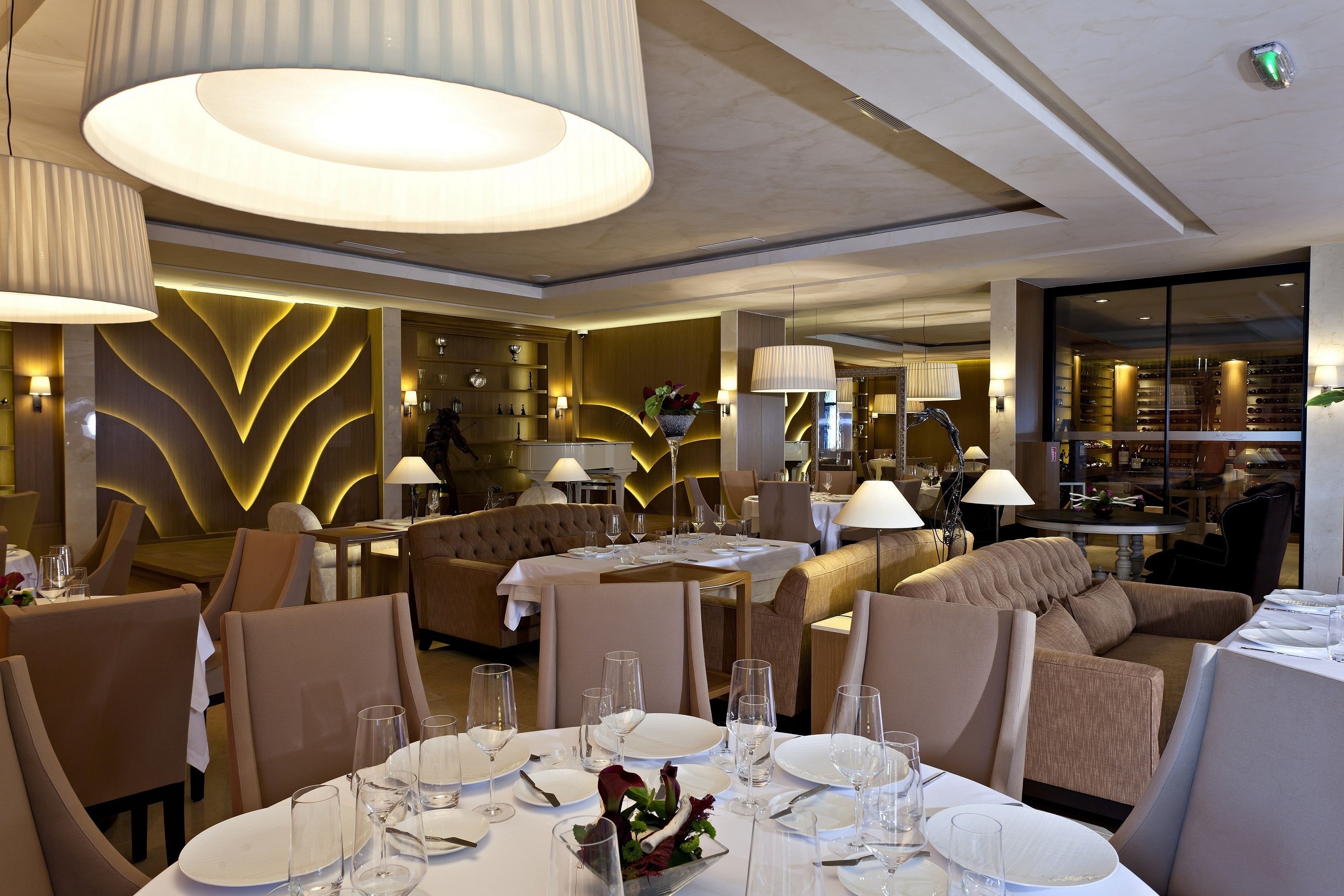A well-lit dining area with round tables, beige upholstered seating, and ambient lighting.