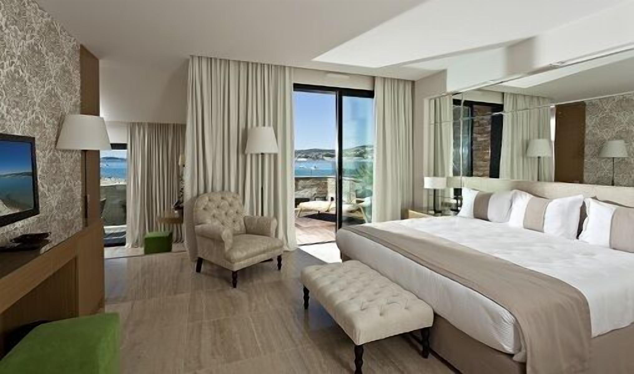 Une chambre d’hôtel avec un grand lit, une chaise, une petite table et une vue sur la mer.