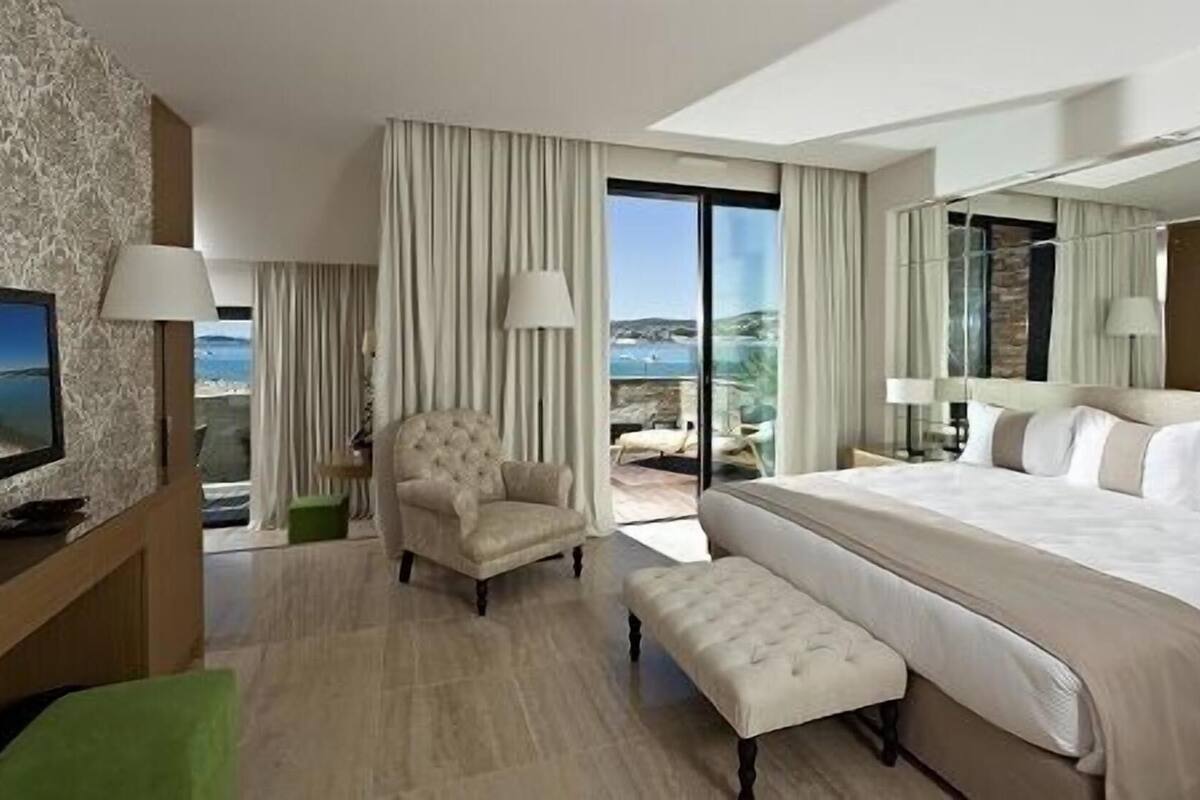 A hotel room with a large bed, a chair, a small table, and a TV.