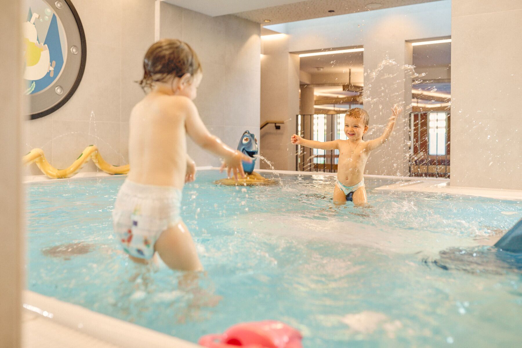 Two children playing in an indoor pool with water jets.