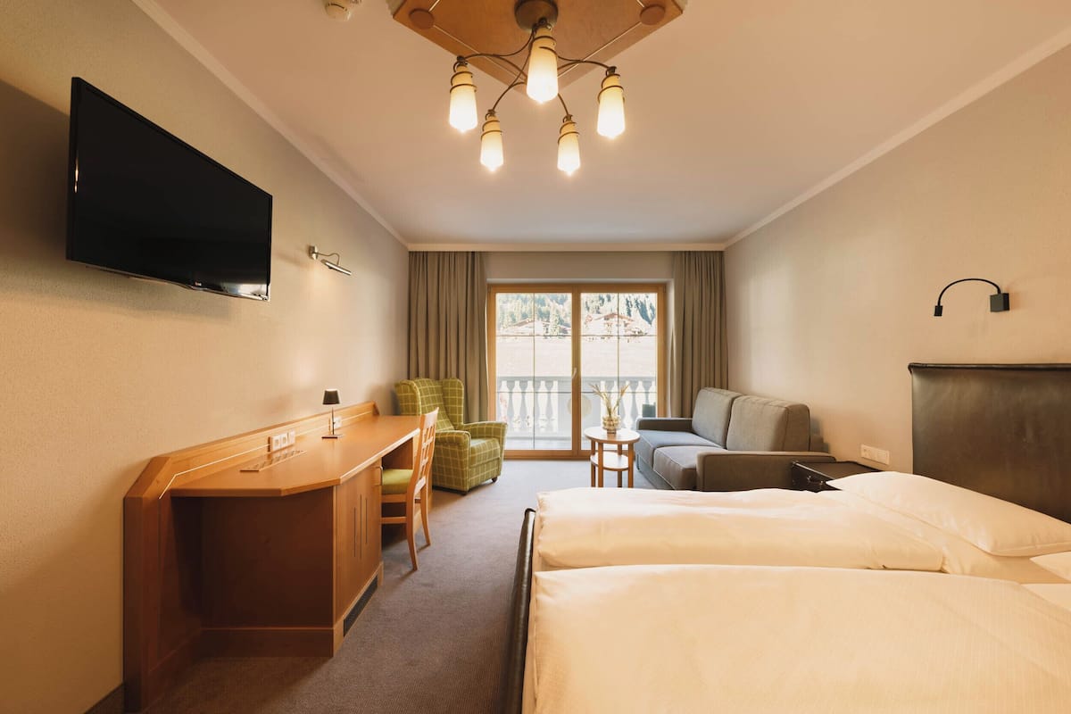 Ein Hotelzimmer mit Bett, Schreibtisch, Stuhl und einem an der Wand befestigten Fernseher.