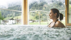 Une personne dans un bain à remous, avec une vue sur un paysage montagneux et des maisons en arrière-plan.