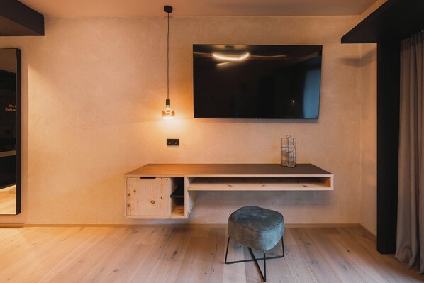 A modern living room with a flat-screen TV mounted on the wall, a wooden console table, a bench, and a hanging light fixture. - Alpenhotel Kindl (Neustift Im Stubaital)