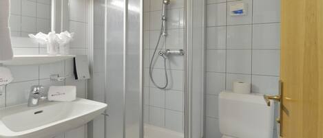 Un baño con lavamanos, espejo, ducha, inodoro y perchero para toallas.