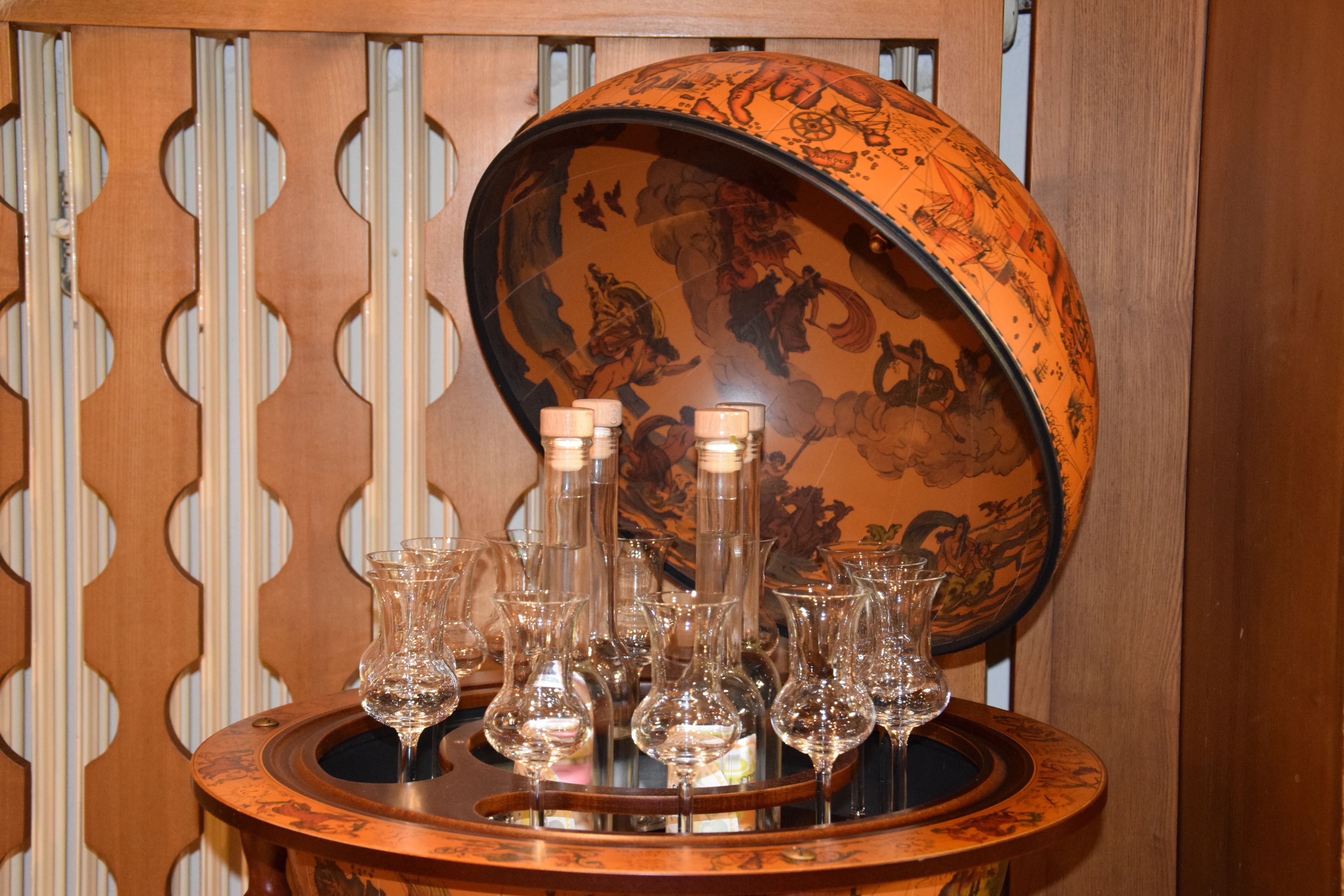 Une table ronde en bois, surmontée d’un couvercle décoratif, sur laquelle sont disposées plusieurs bouteilles et verres à vin en verre transparent.