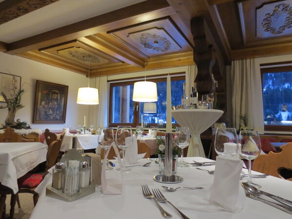 A dining area with tables set for a meal, featuring a central decorative piece, candles, and wine glasses.