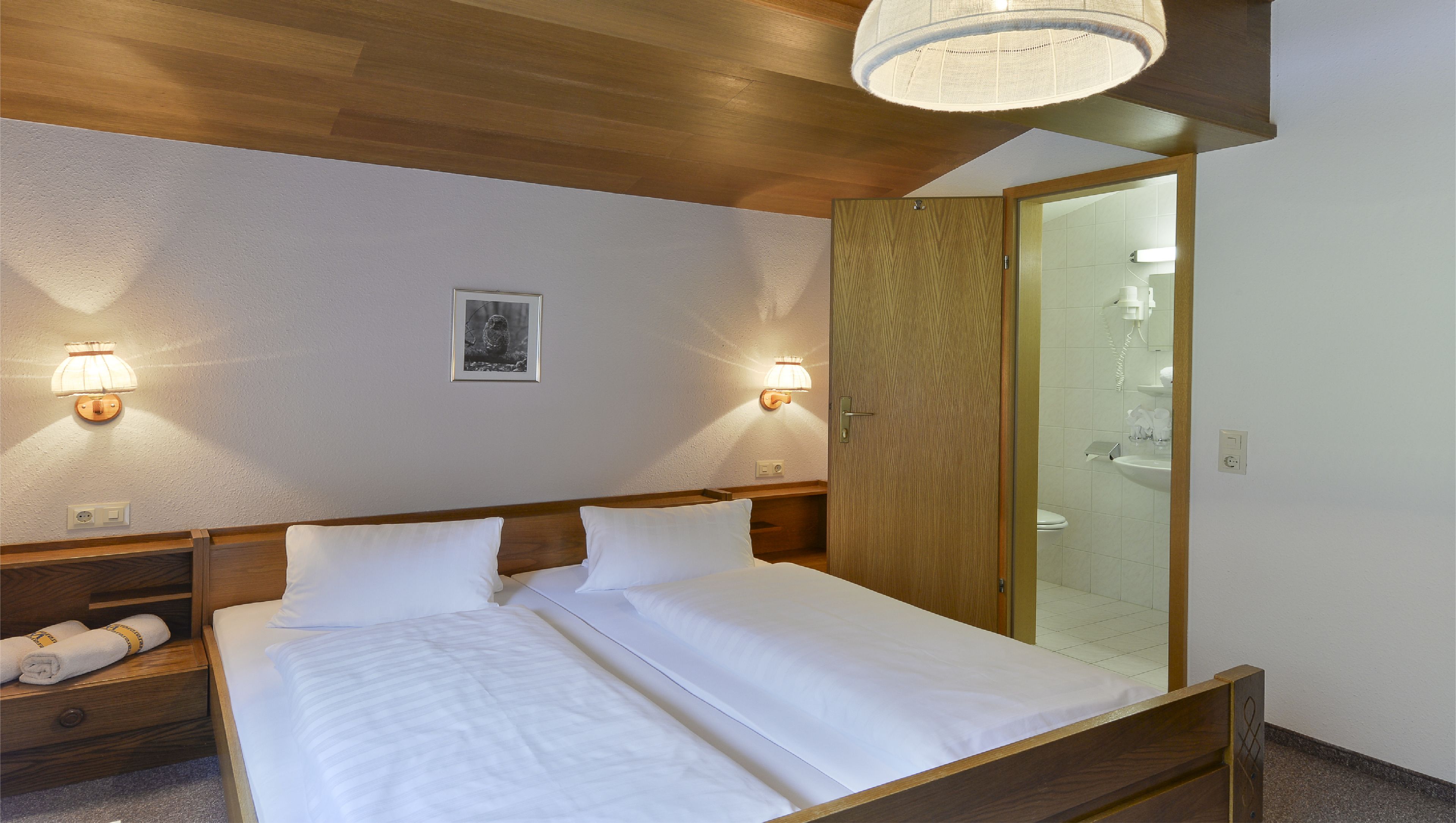 A hotel room with a wooden bed, two bedside lamps, a framed picture on the wall, and a large mirror.