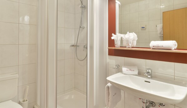 A modern bathroom with a shower, toilet, and sink. There are towels and toiletries on the sink counter. - Hotel Sonnblick (Dalaas)