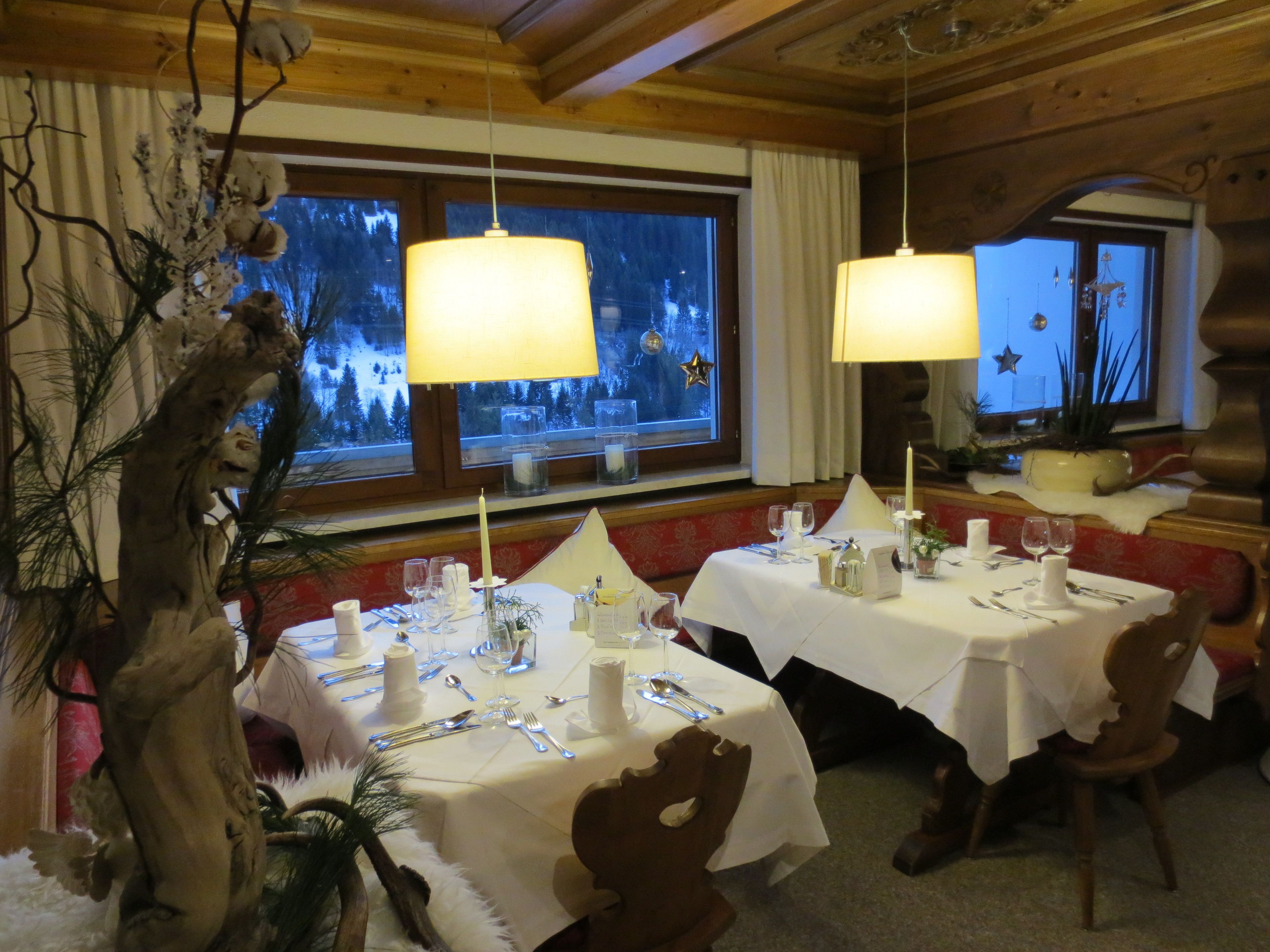 Un coin repas chaleureux aux murs en bois, avec une fenêtre donnant sur un paysage enneigé. Les tables sont dressées avec des nappes blanches, des bougies et des couverts.