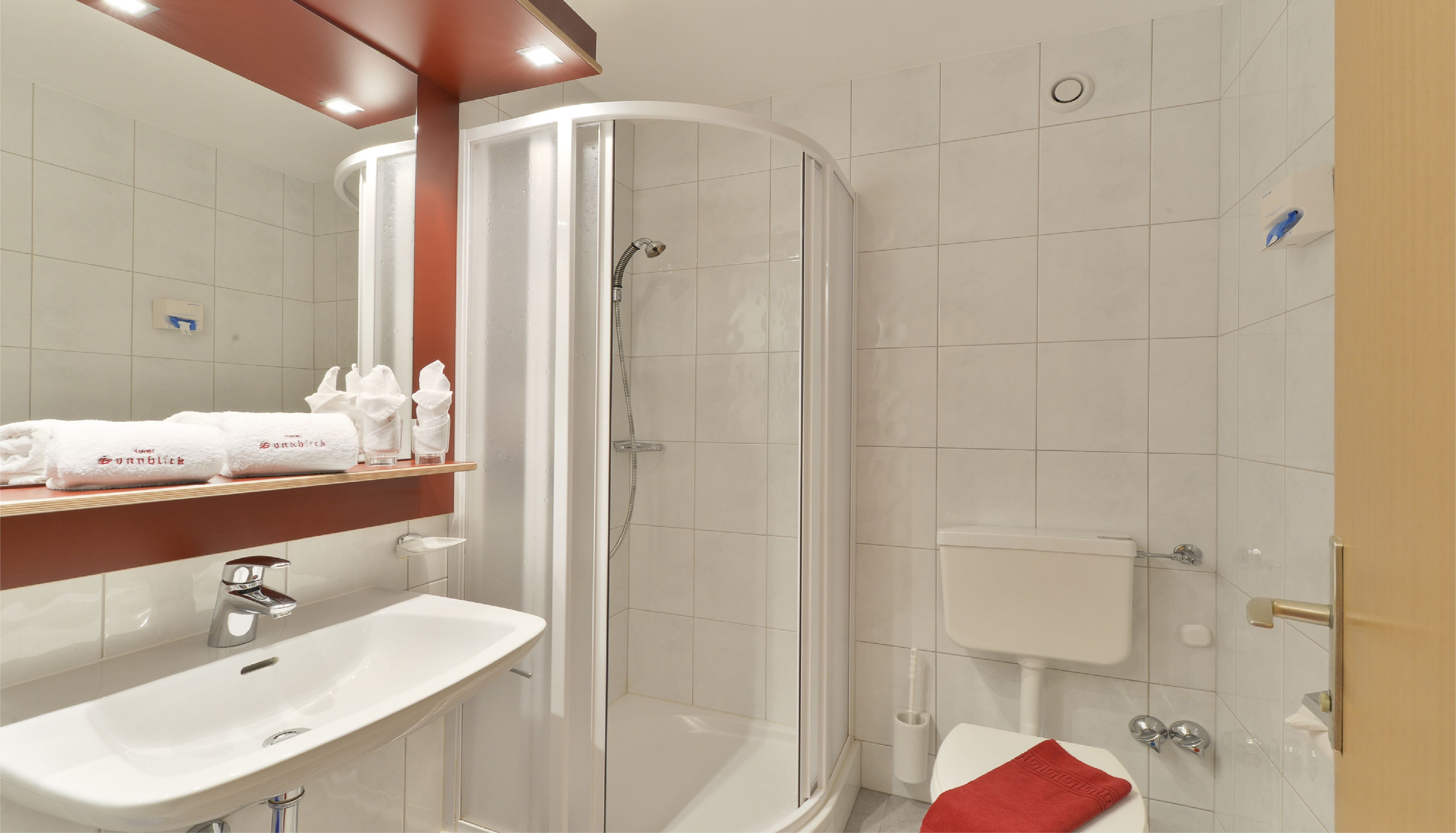 Un baño moderno con lavamanos, espejo, toallero, ducha, inodoro y una toalla sobre el inodoro.