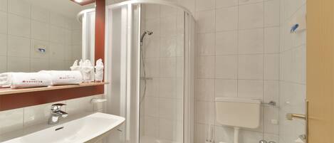 Un baño moderno con lavamanos, espejo, toallero, ducha, inodoro y una toalla sobre el inodoro.