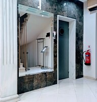 Um hall moderno com piso de mármore, elevador de vidro, extintor de incêndio e um suporte de metal para informações.