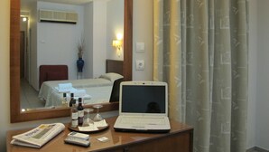 Une chambre d’hôtel avec un lit, un bureau avec un ordinateur portable, un miroir et une fenêtre avec des rideaux.