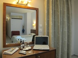 Quarto de hotel com cama, escrivaninha, laptop, espelho e janela com cortinas.
