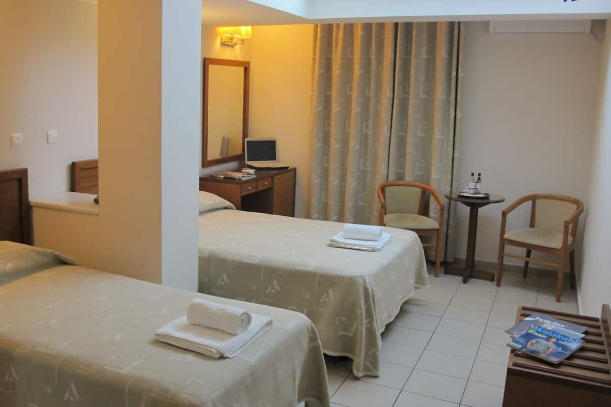 Une chambre d’hôtel avec deux lits, un bureau avec un ordinateur, une chaise et une petite table avec des magazines.