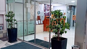 L’entrée d’un hôtel avec des portes vitrées, des plantes en pot, un comptoir d’accueil et un panneau indiquant clairement la sortie.