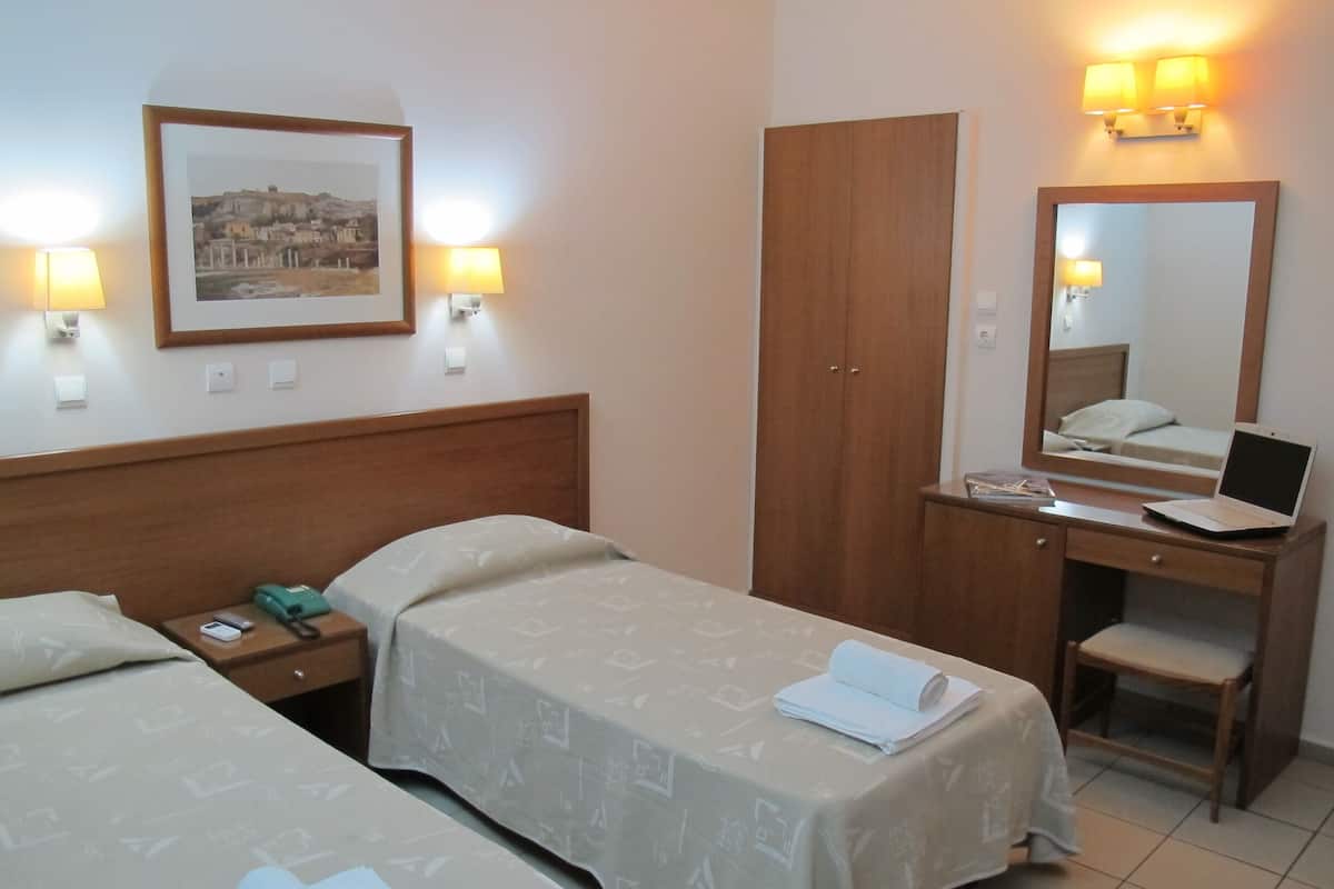 Une chambre d’hôtel avec deux lits, un bureau avec un ordinateur portable, une armoire et une lampe de chevet.