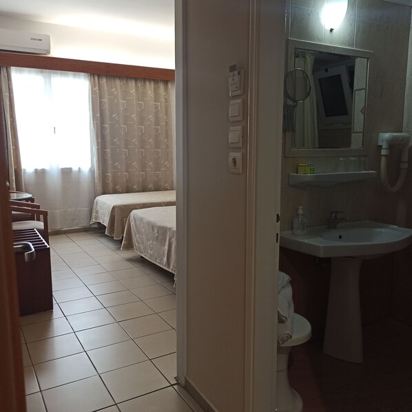 A hotel room with a bed, a small table, a sink, and a mirror.