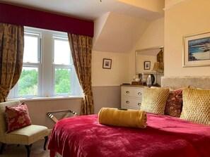 A bedroom with a bed, a chair, a dresser, and a window with curtains. - Maple Bank (Keswick)