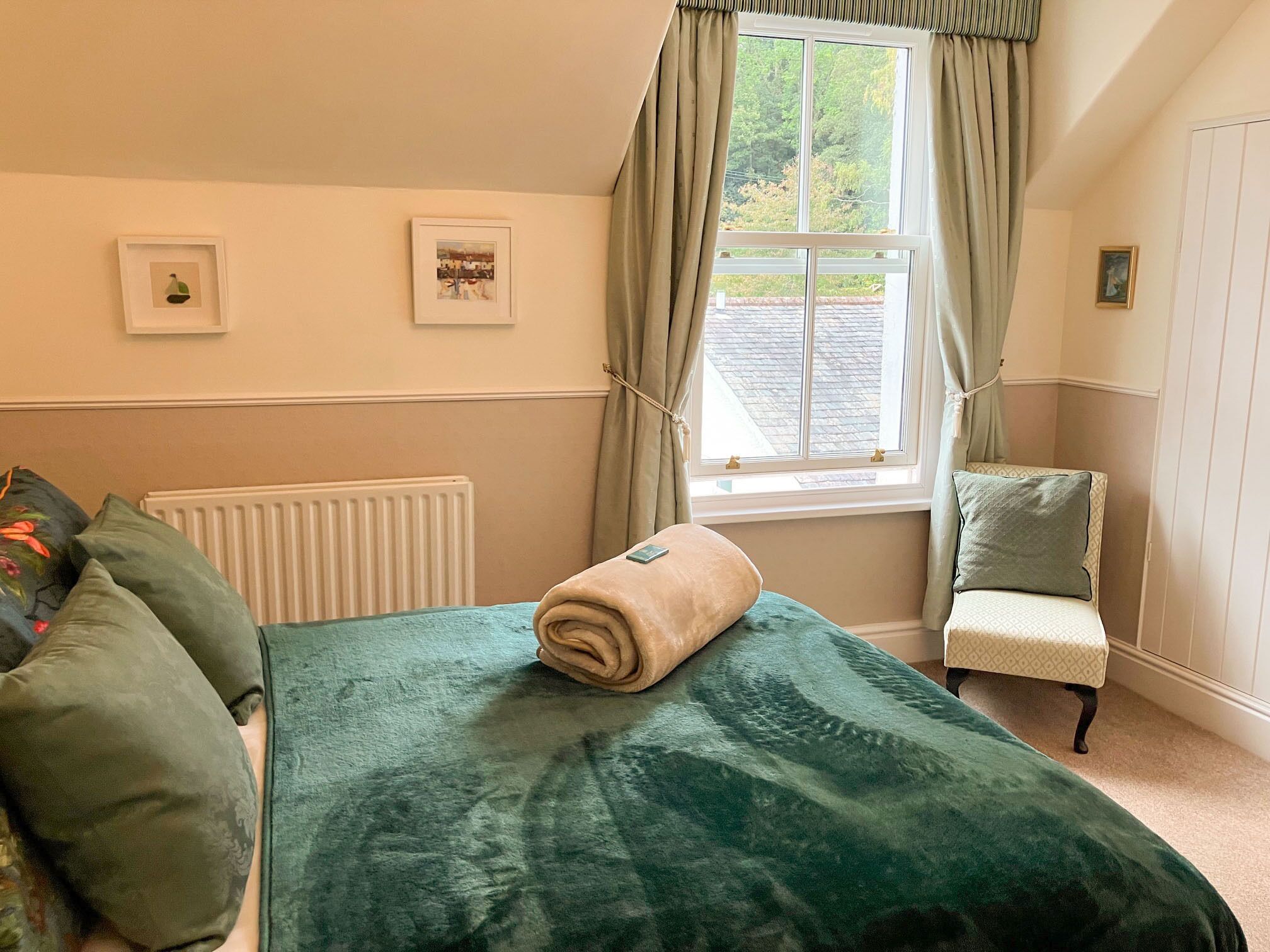 A bedroom with a large bed, a chair, a radiator, and a window with curtains.